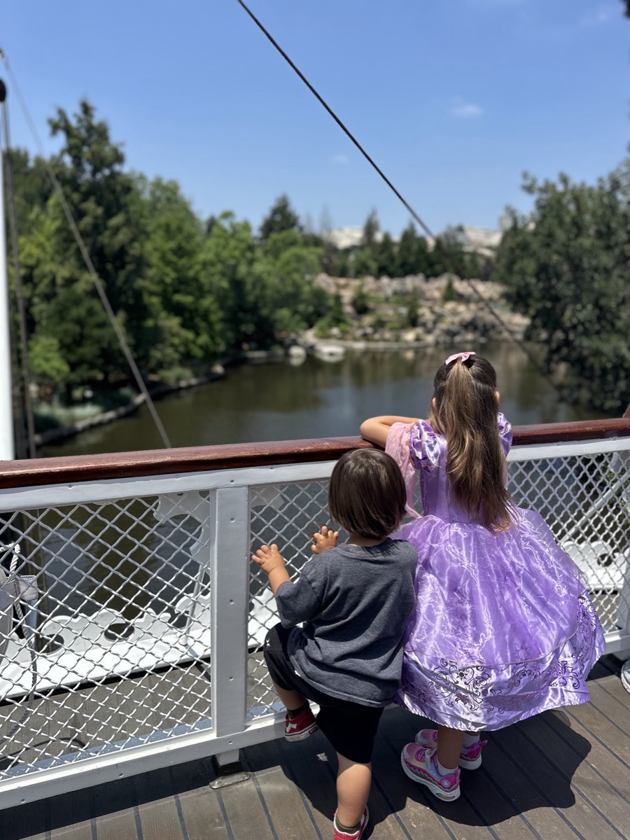 Two children leaning on a riverboat railing, looking out over the water